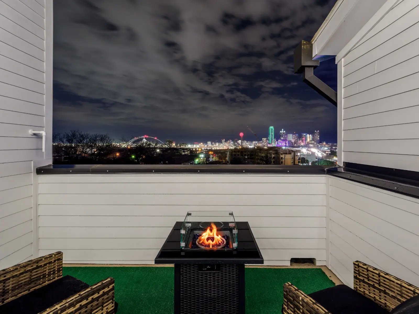 A modern rooftop with comfy seating, turf flooring, and a sleek fire pit—perfect for relaxing with stunning nighttime skyline views.